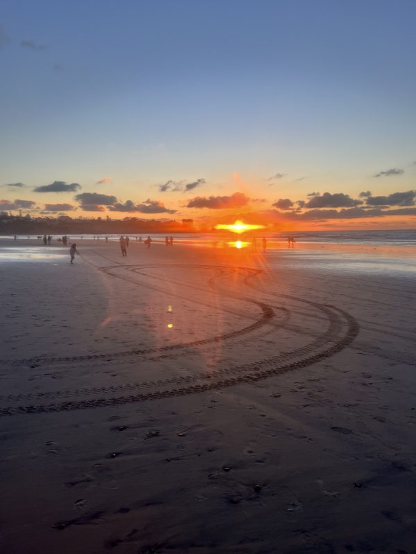 Right before sunset with brilliant orange flare over the sand with tracks in it and a clear sky